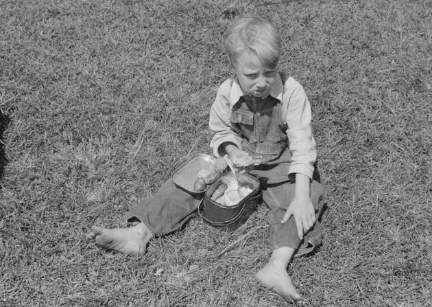image of a boy in overalls sitting on the grass eating lunch